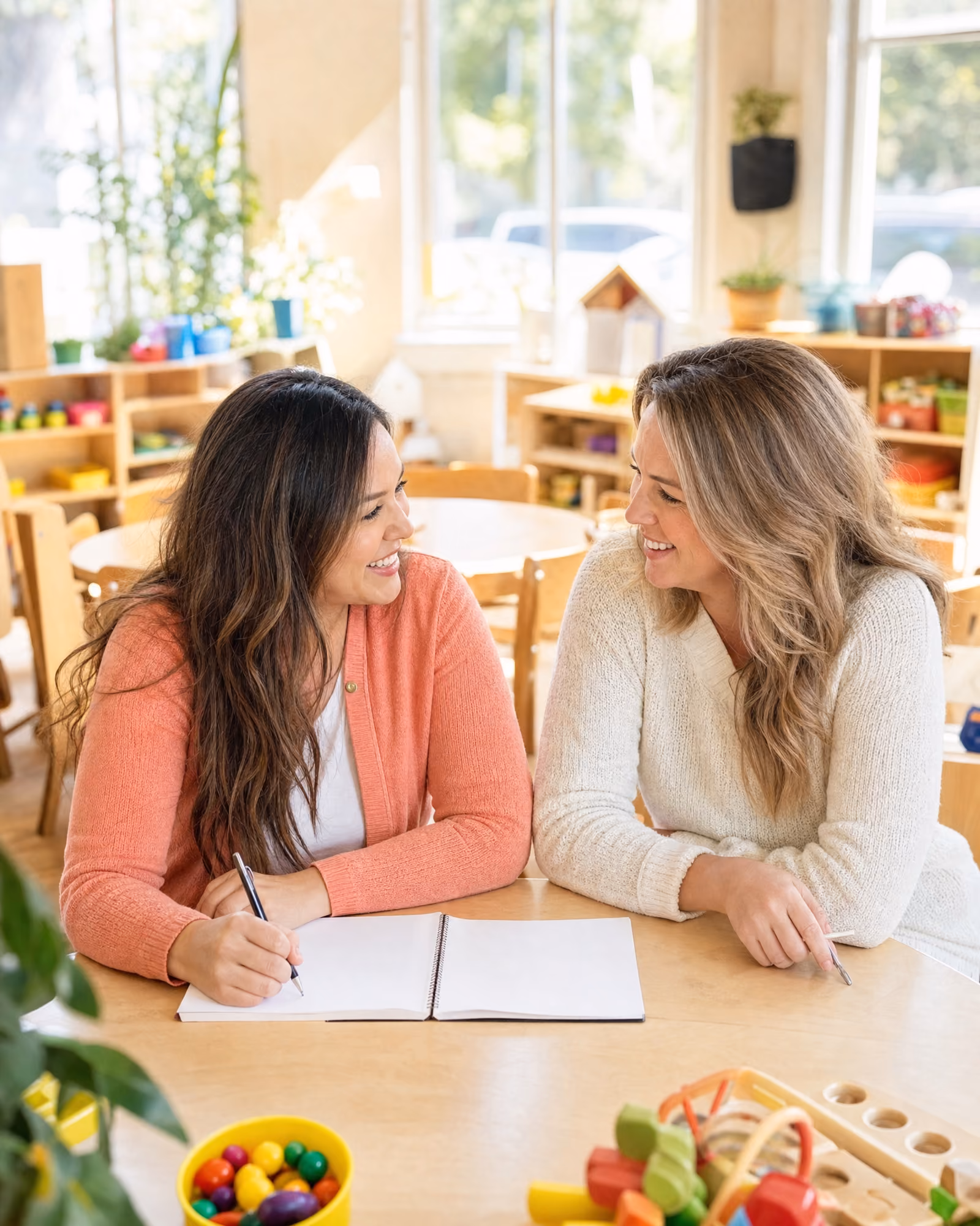 A behavior consultant and a teacher sitting together at a classroom table, collaborating over blank notes.