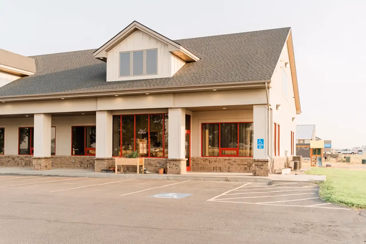 Covered entrance of the Idaho Falls clinic, a beige building with brick trim, red-framed windows, and a playground to the side.