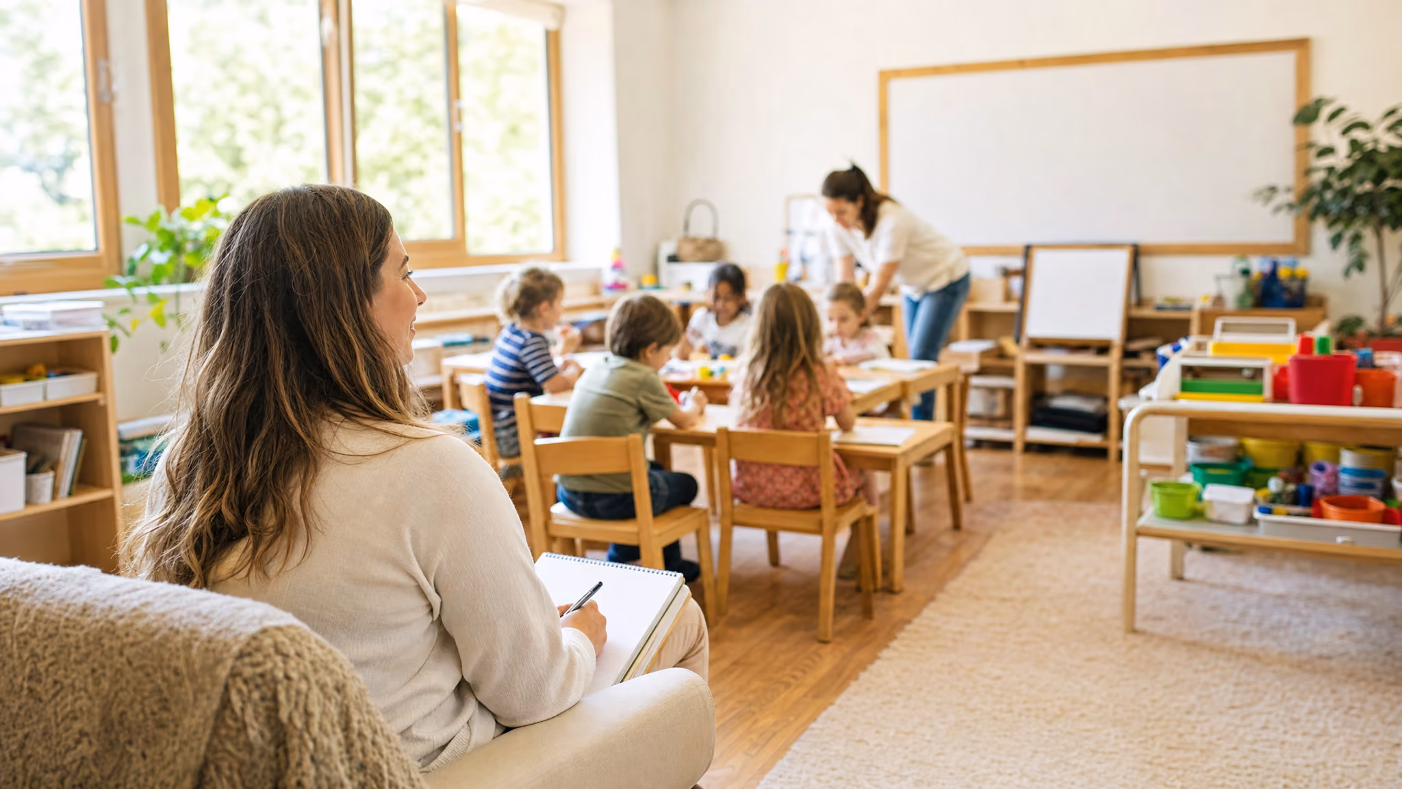 An observer seated at the back of a classroom taking notes while a lesson goes on in the foreground.