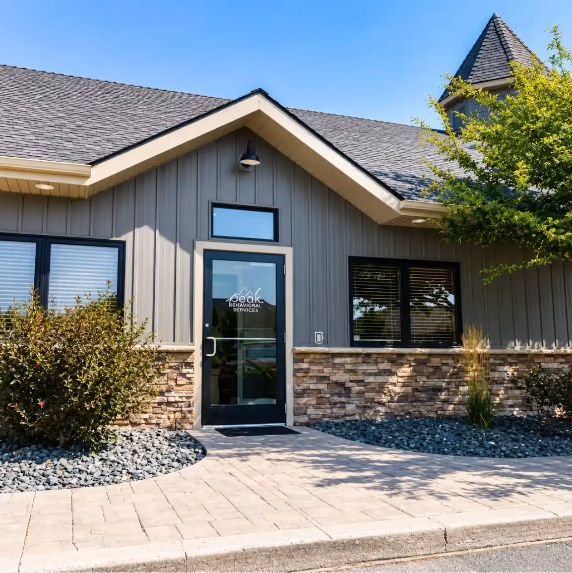 Stone and siding exterior of Peak Behavioral Services in Rexburg, Idaho, with a glass entrance and the mountain logo on the door.
